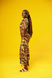 Woman wearing wide leg African palazzo pants with a geometric brown, yellow, orange, and black print. The cropped trousers are made from lightweight cotton, styled as part of a festival outfit with a matching wrap crop top.