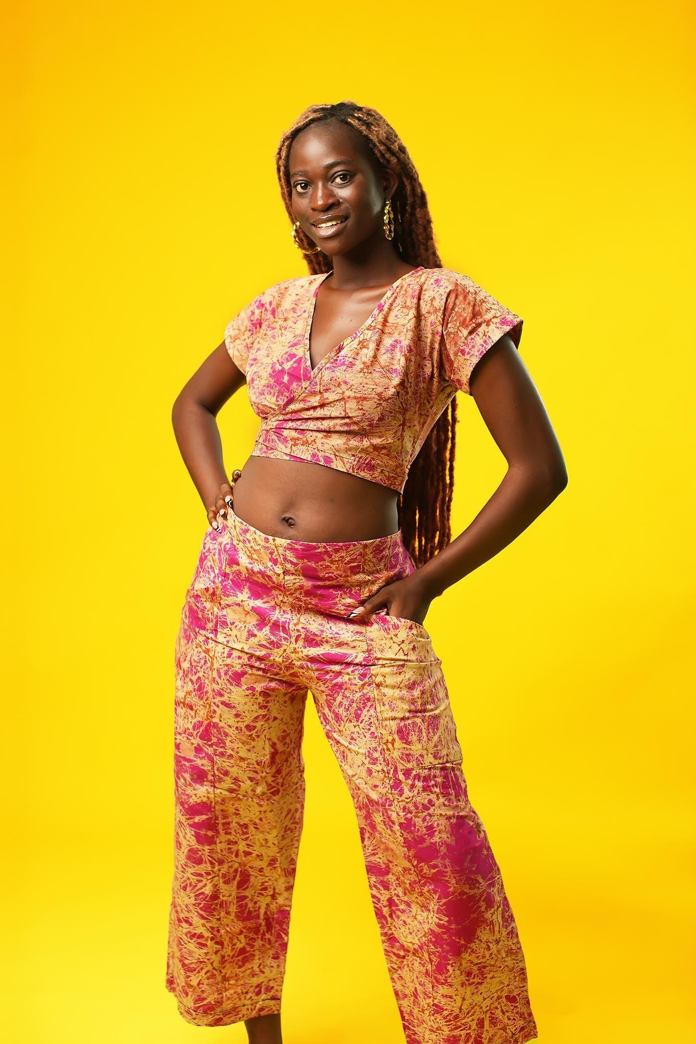 Woman wearing pink and cream batik wide-leg culotte trousers made from cotton fabric. The palazzo pants have a high waist, side pockets, and cropped length, styled as part of a matching two-piece set.