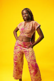 Woman wearing pink and cream batik wide-leg culotte trousers made from cotton fabric. The palazzo pants have a high waist, side pockets, and cropped length, styled as part of a matching two-piece set.