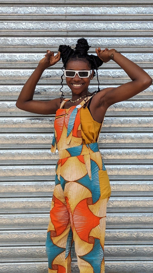 Woman in a colourful patterned dungarees standing in front of a metal shutter.