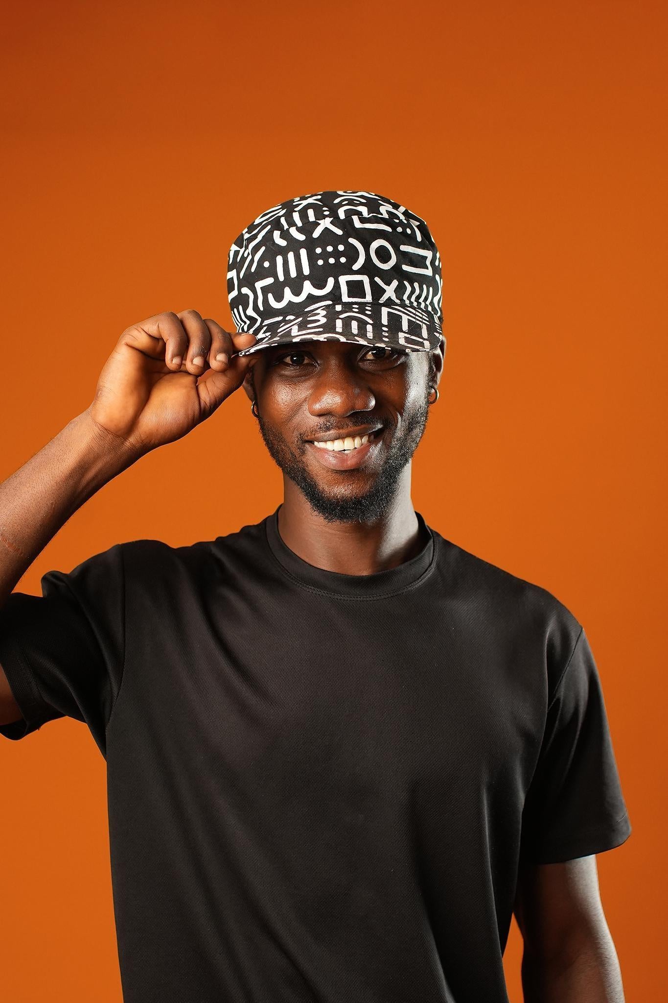 Close-up of a man wearing a Black and White Baseball Cap made from 100% cotton, featuring a Mudcloth Afrocentric print. The unisex cap has a flat brim and bold tribal symbols, styled as a Bohemian Tribal Festival accessory or African Gift.