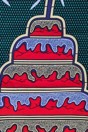 Bold and colourful African wax print fabric featuring a repeating pattern of tiered birthday cakes with red, white, and blue icing and a single lit candle on top. The background is a deep green with a small geometric triangle pattern, and the cakes are arranged upright and upside down in an alternating design.
