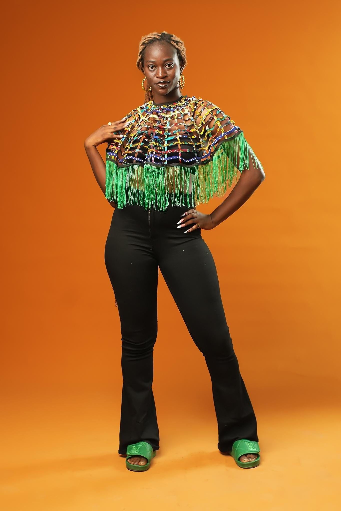 Woman wearing a Green Tassel Cape made from recycled African print fabric, styled as a bold Ankara Cape. This colourful Festival Outfit piece is perfect for Afropunk events, Rave Wear or adding flair to any look—crafted by Ashanti Empress.