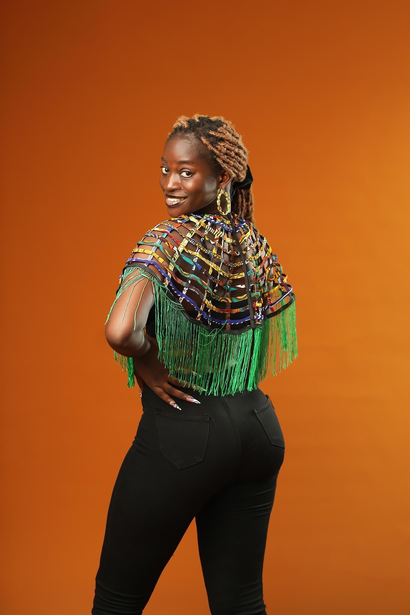 Woman wearing a Green Tassel Cape made from recycled African print fabric, styled as a bold Ankara Cape. This colourful Festival Outfit piece is perfect for Afropunk events, Rave Wear or adding flair to any look—crafted by Ashanti Empress.