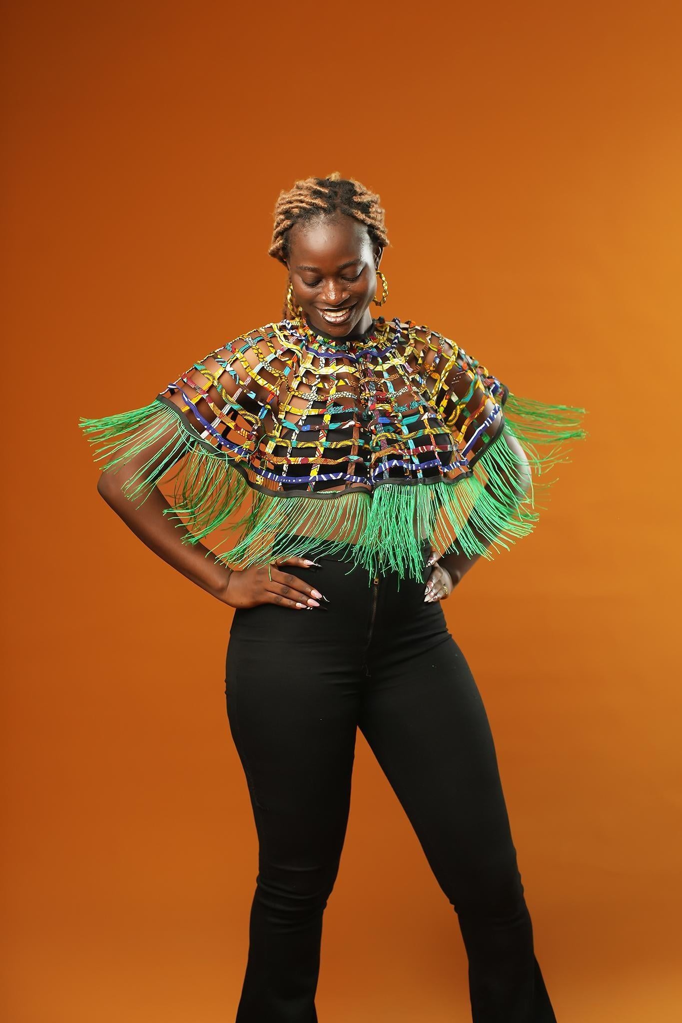 Woman wearing a Green Tassel Cape made from recycled African print fabric, styled as a bold Ankara Cape. This colourful Festival Outfit piece is perfect for Afropunk events, Rave Wear or adding flair to any look—crafted by Ashanti Empress.