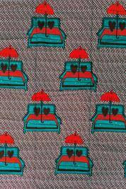 African wax print fabric featuring a playful and romantic design of turquoise blue sofas with red and brown heart-shaped pillows, each topped with a bright red umbrella. The background is a dark brown covered in a pattern of small white teardrop shapes, creating a bold and eye-catching contrast. Perfect for statement fashion or unique home decor projects.