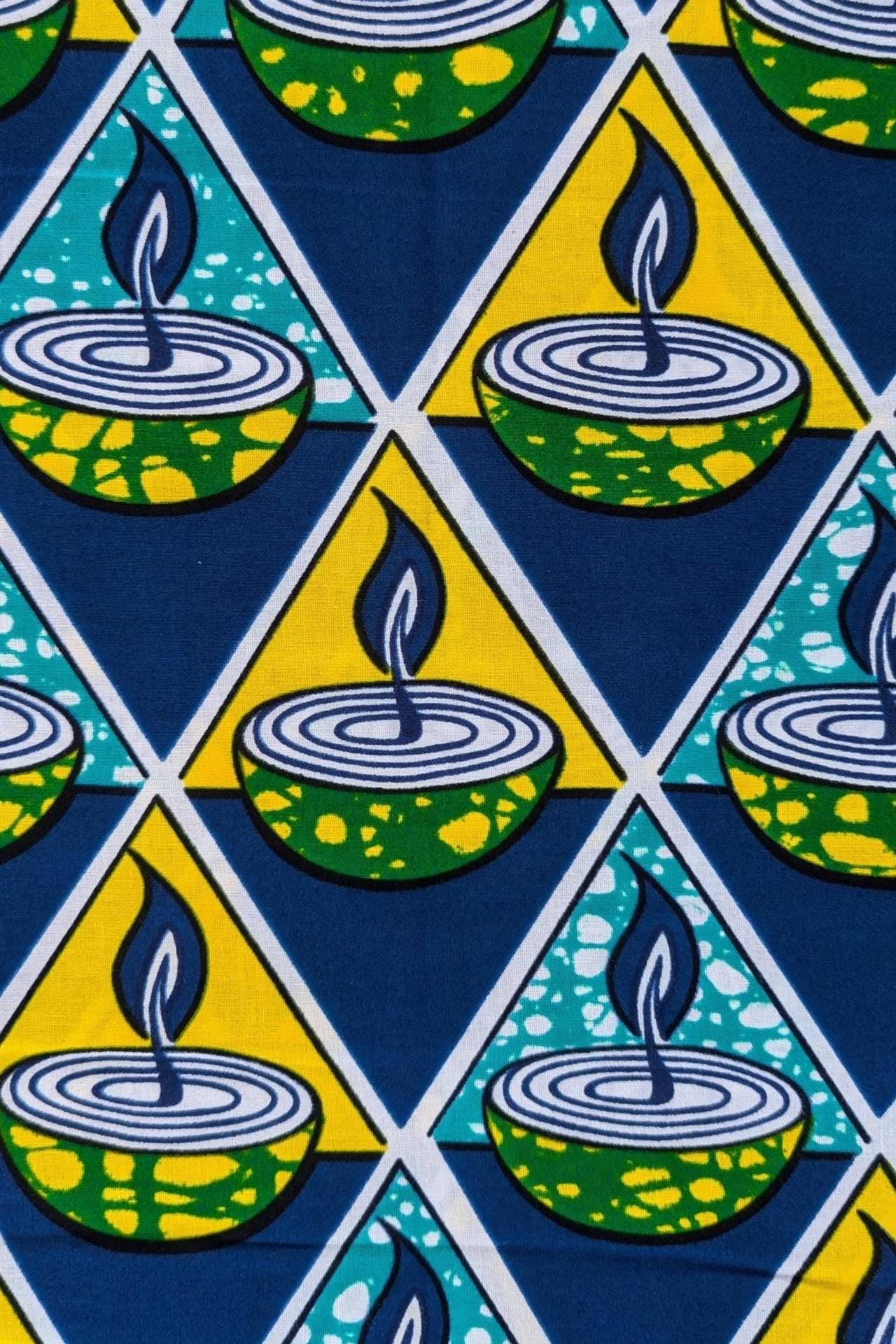 Bold African wax print fabric featuring a repeating pattern of green and yellow candle bowls with blue flames, set inside alternating teal and yellow triangles on a dark blue background.