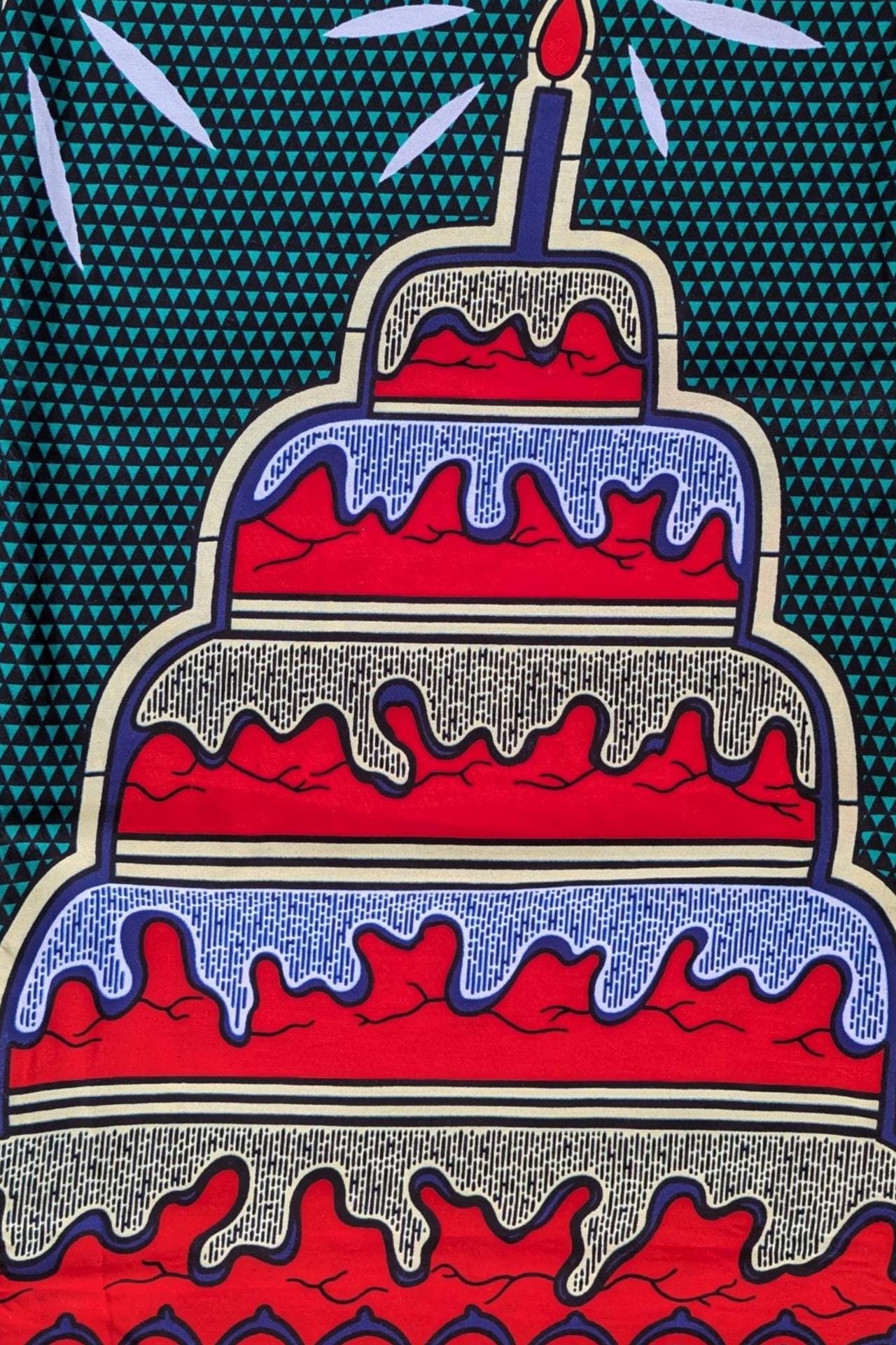 Bold and colourful African wax print fabric featuring a repeating pattern of tiered birthday cakes with red, white, and blue icing and a single lit candle on top. The background is a deep green with a small geometric triangle pattern, and the cakes are arranged upright and upside down in an alternating design.