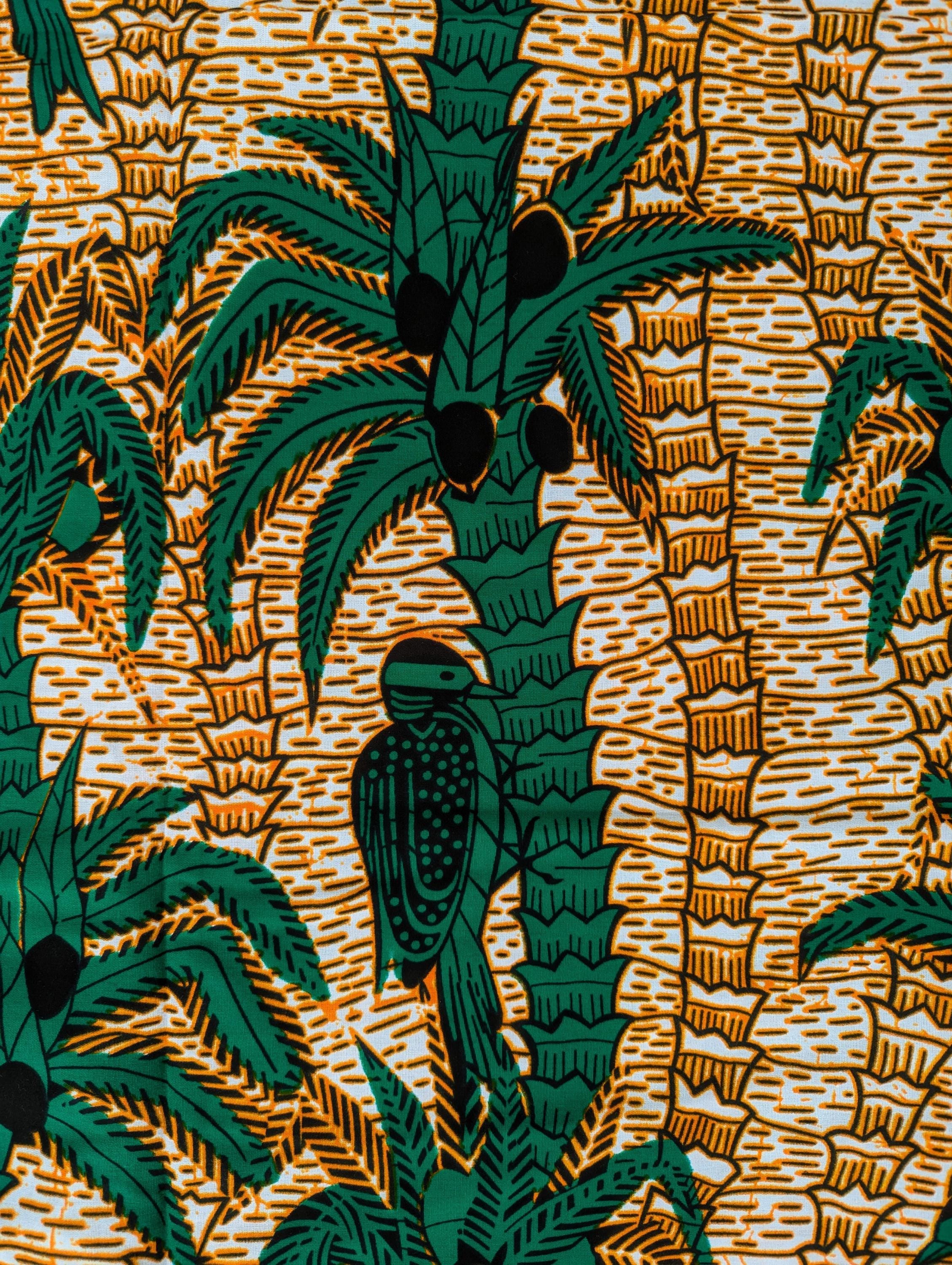 Tropical-themed African wax print fabric featuring green palm trees with coconuts and perched birds, set against a warm background of textured golden-brown lines. The repeating pattern creates a lush, jungle-like feel, perfect for vibrant fashion, home decor, or craft projects.