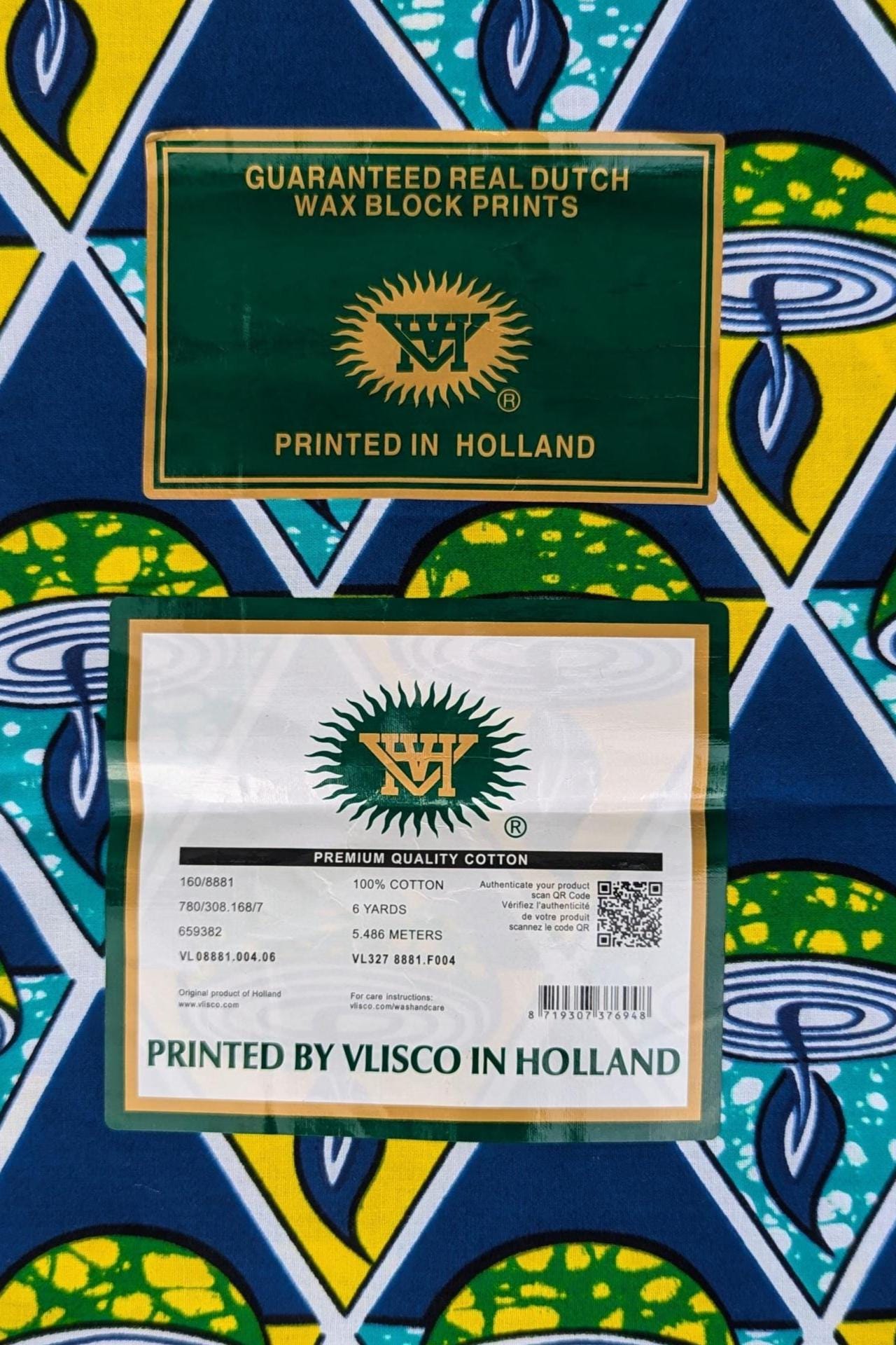 Bold African wax print VLISCO fabric featuring a repeating pattern of green and yellow candle bowls with blue flames, set inside alternating teal and yellow triangles on a dark blue background.