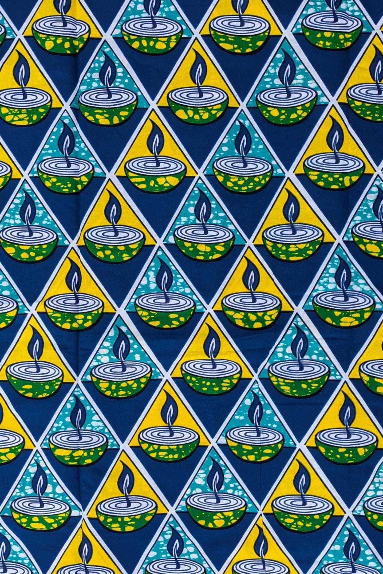 Bold African wax print fabric featuring a repeating pattern of green and yellow candle bowls with blue flames, set inside alternating teal and yellow triangles on a dark blue background.