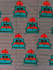African wax print fabric featuring a playful and romantic design of turquoise blue sofas with red and brown heart-shaped pillows, each topped with a bright red umbrella. The background is a dark brown covered in a pattern of small white teardrop shapes, creating a bold and eye-catching contrast. Perfect for statement fashion or unique home decor projects.