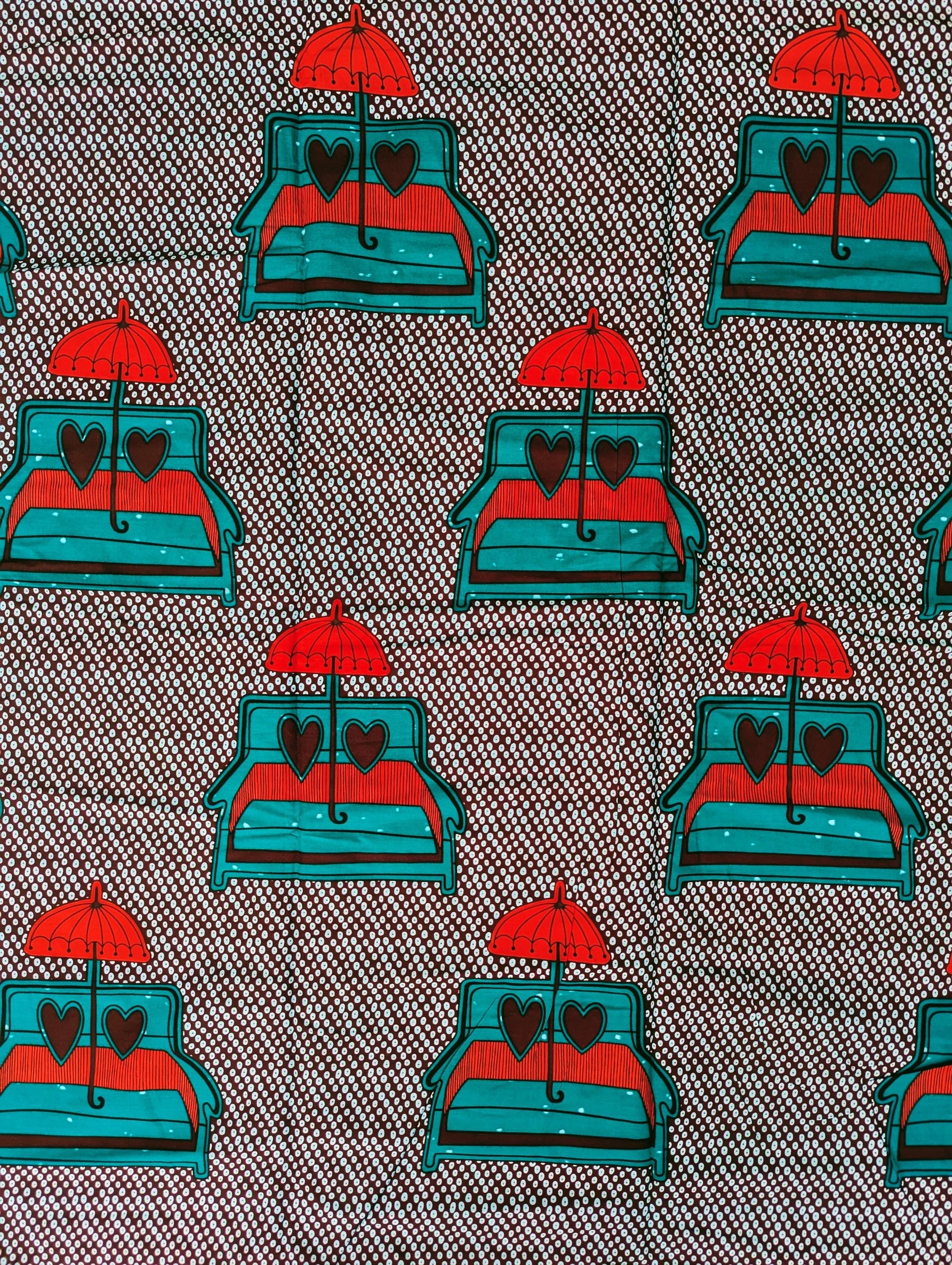 African wax print fabric featuring a playful and romantic design of turquoise blue sofas with red and brown heart-shaped pillows, each topped with a bright red umbrella. The background is a dark brown covered in a pattern of small white teardrop shapes, creating a bold and eye-catching contrast. Perfect for statement fashion or unique home decor projects.