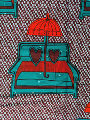 African wax print fabric featuring a playful and romantic design of turquoise blue love seats with red and brown heart-shaped pillows, each topped with a bright red umbrella. The background is a dark brown covered in a pattern of small white teardrop shapes, creating a bold and eye-catching contrast. Perfect for statement fashion or unique home decor projects.