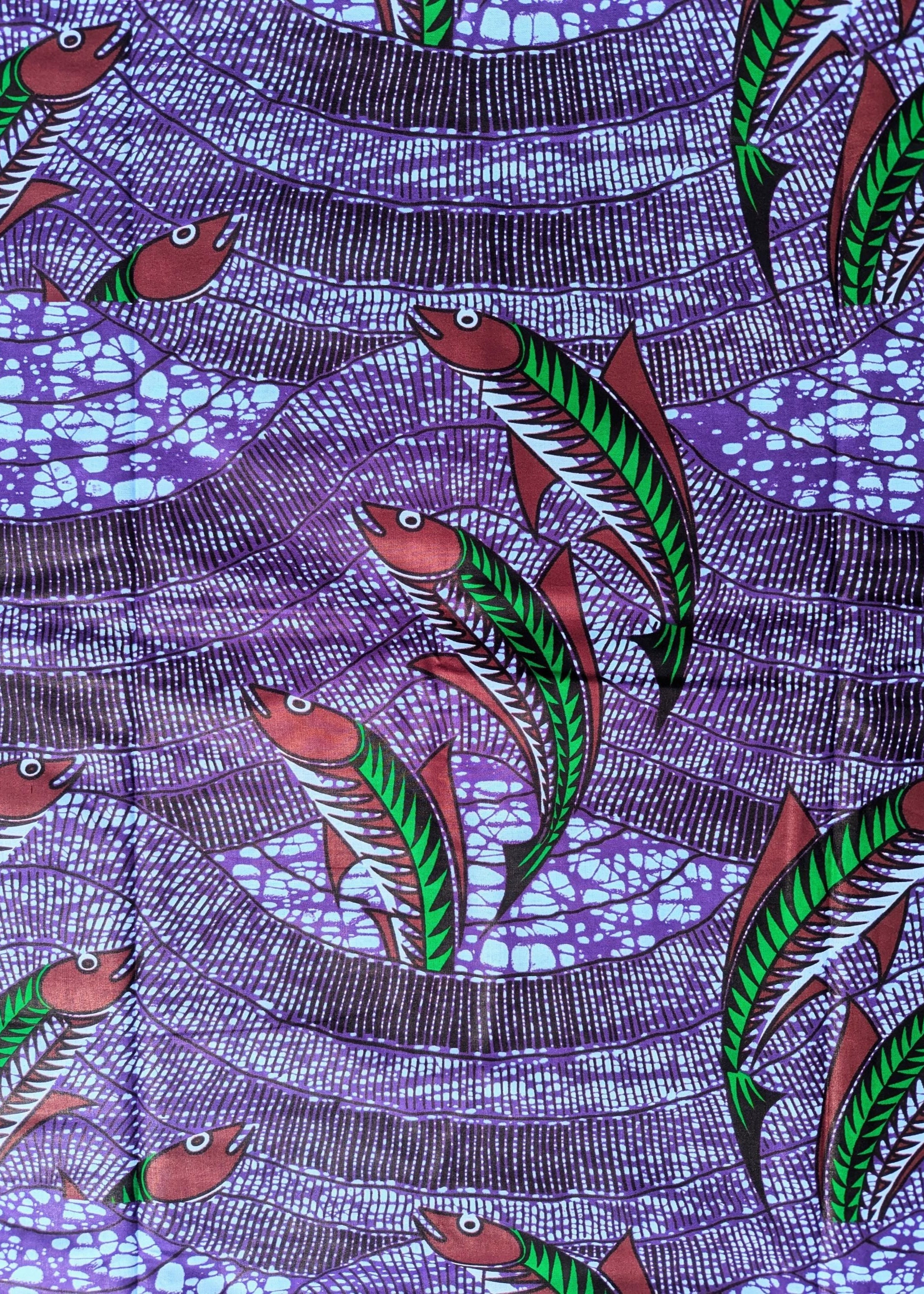 Vibrant African wax print fabric featuring a dynamic underwater scene of green and red fish swimming through wavy purple and blue waters. The background has a textured pattern resembling flowing currents and bubbles, adding movement and depth to the design. Perfect for bold fashion or aquatic-themed crafts.