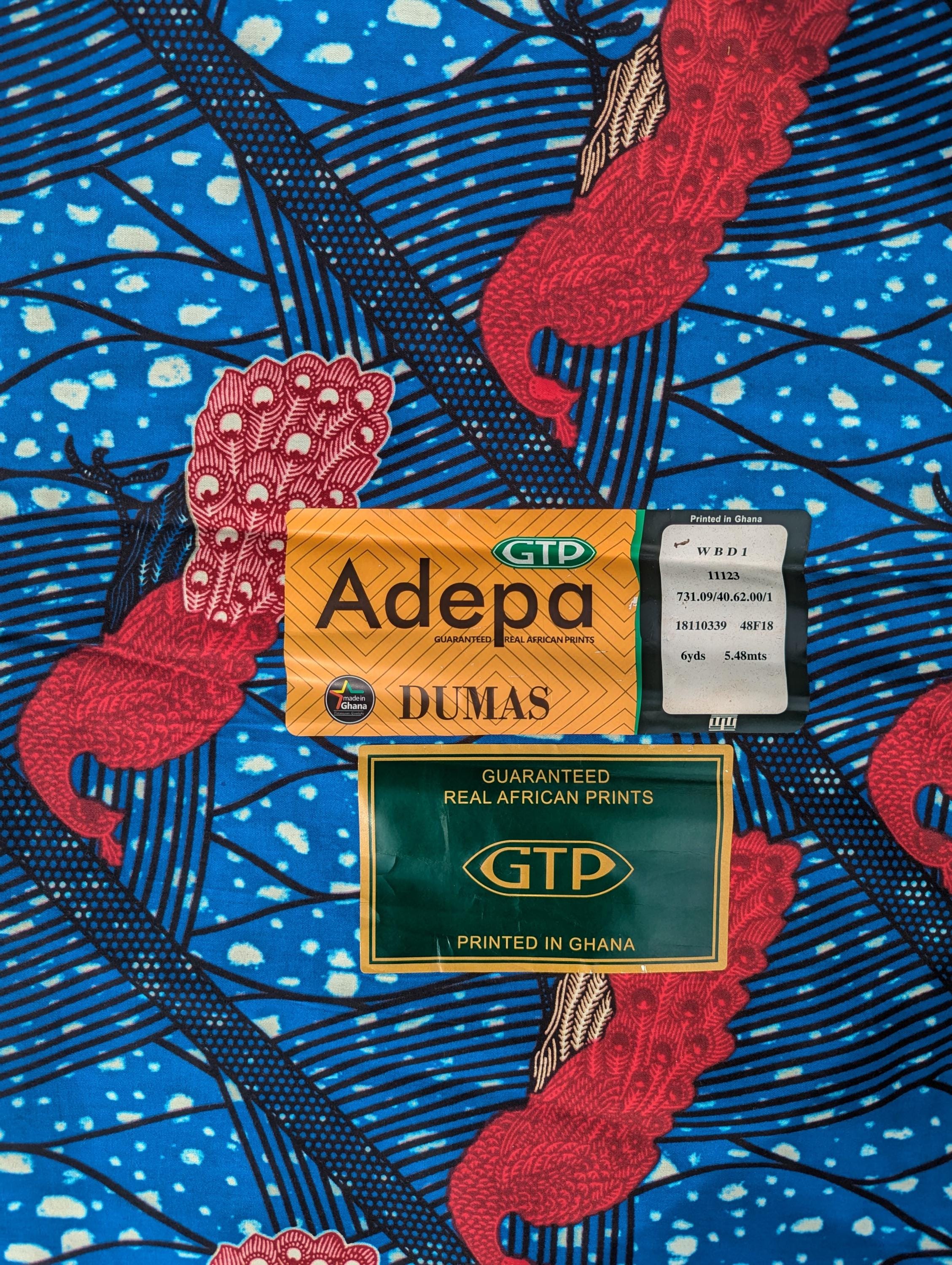 Bright and bold African wax print fabric made by GTP (Ghana Textile Production) It features elegant pink peacocks with intricately patterned tail feathers standing against a vivid blue background. The design includes diagonal black lines and abstract wave-like patterns with splashes of cream, creating a striking contrast and sense of movement. Perfect for standout fashion pieces or statement accessories.