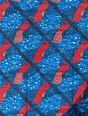 Bright and bold African wax print fabric featuring elegant pink peacocks with intricately patterned tail feathers standing against a vivid blue background. The design includes diagonal black lines and abstract wave-like patterns with splashes of cream, creating a striking contrast and sense of movement. Perfect for standout fashion pieces or statement accessories.
