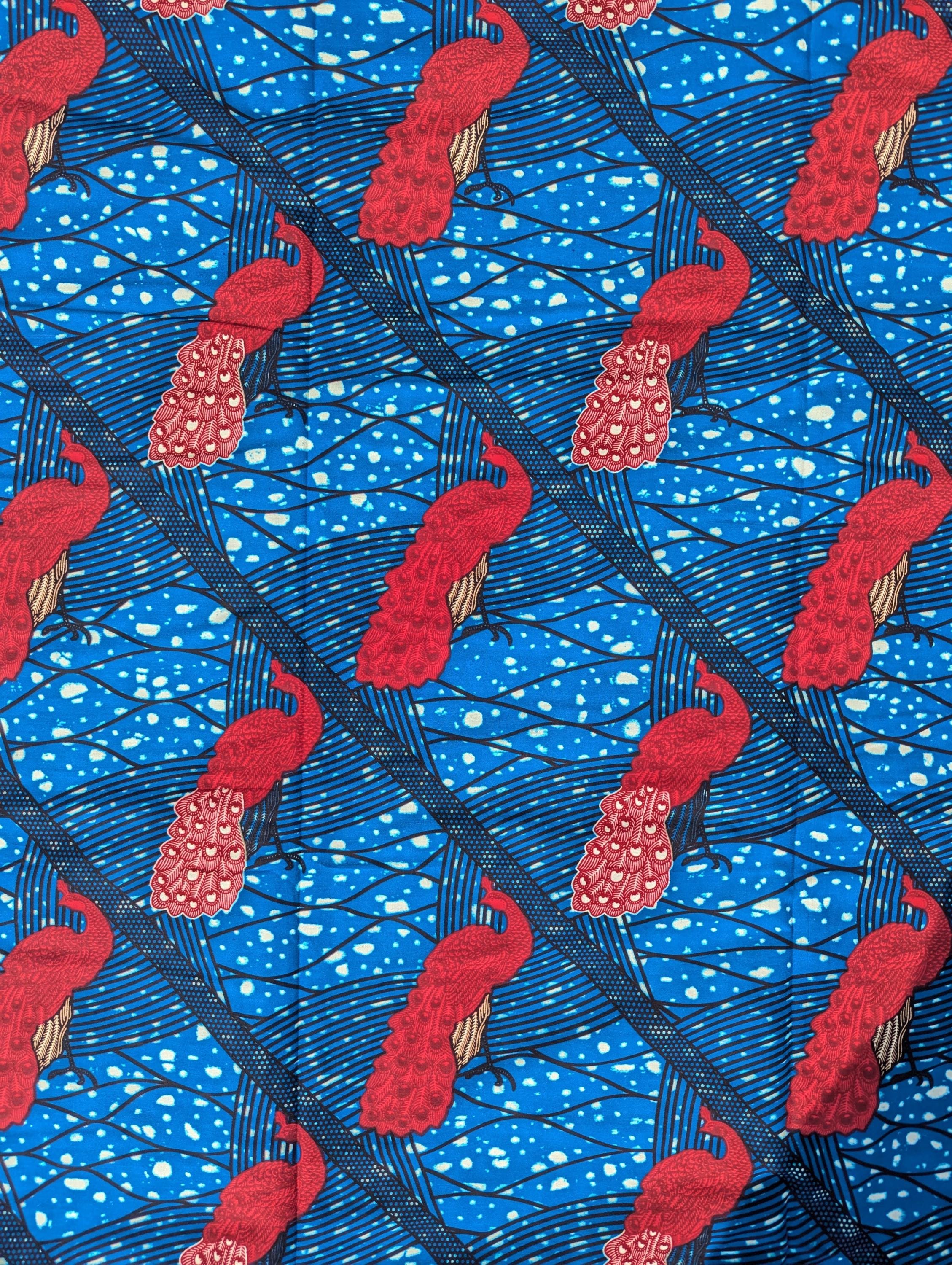 Bright and bold African wax print fabric featuring elegant pink peacocks with intricately patterned tail feathers standing against a vivid blue background. The design includes diagonal black lines and abstract wave-like patterns with splashes of cream, creating a striking contrast and sense of movement. Perfect for standout fashion pieces or statement accessories.