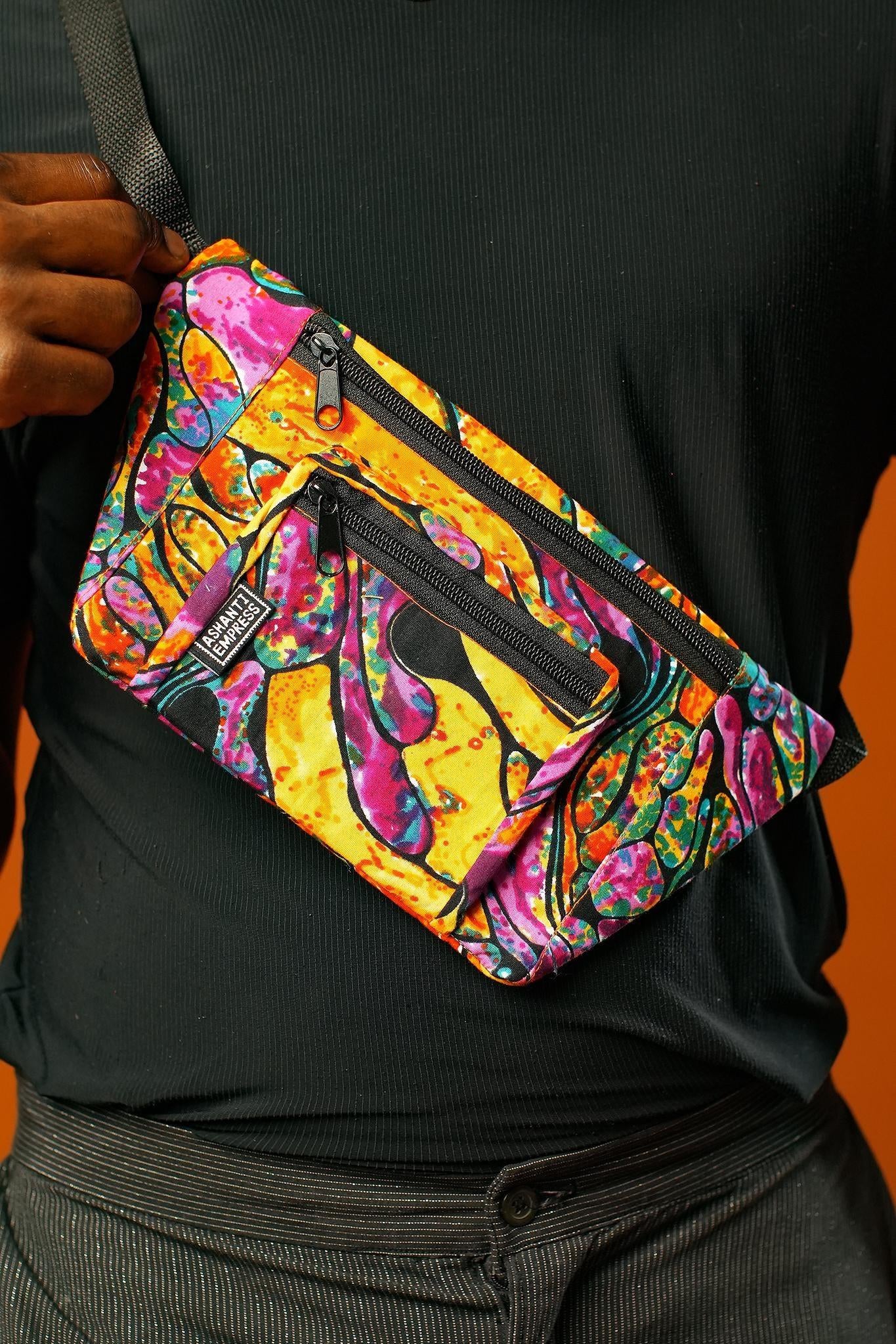 Close-up of a person wearing a Psychedelic Rave Bum Bag made from colourful Ankara fabric, worn crossbody style. The Fanny Pack features three zip compartments and bold orange, purple, and green patterns, designed as a Boho Hip Bag or Festival Bag for vibrant festival outfits.