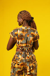 Woman wearing wide leg African palazzo pants with a geometric brown, yellow, orange, and black print. The cropped trousers are made from lightweight cotton, styled as part of a festival outfit with a matching wrap crop top.