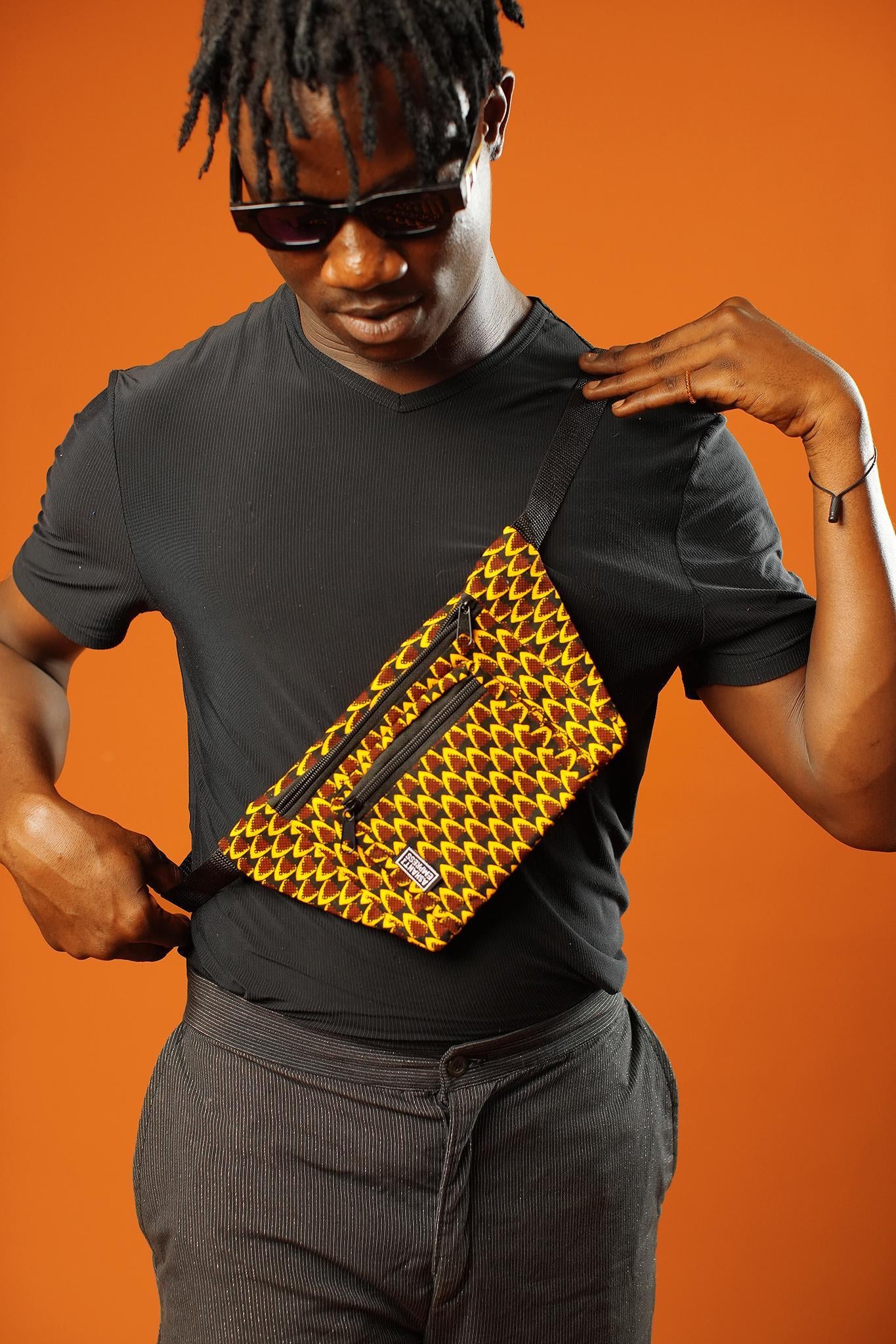 Man wearing an Orange Bum Bag across the chest, styled as a Colourful Cross Body Bag. The Fanny Pack features bold yellow and red Ankara print, two zip pockets, and black strap—perfect as a Festival Bag or Boho Hip Bag from Ashanti Empress.