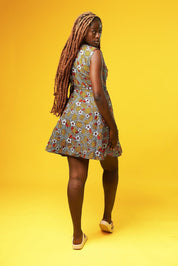 Woman wearing a sleeveless African print wrap dress made from colourful ankara fabric with yellow, red, and white floral patterns. The dress features a V-neckline and tie waist, and falls above the knees.