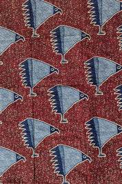 African wax print fabric with a striking pattern of stylised blue birds resembling eagles or hawks, each standing on one leg. The birds are illustrated in a speckled texture with navy and sky blue wings, set against a rich red background filled with small, abstract cream and black shapes. Bold and graphic, this fabric is ideal for statement fashion or unique accessories.